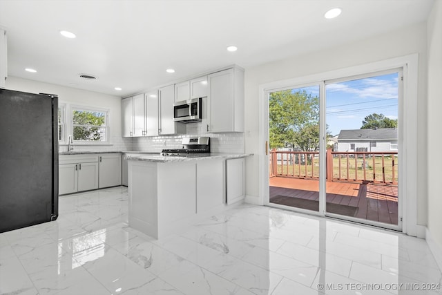 kitchen featuring stainless steel appliances, sink, kitchen peninsula, backsplash, and white cabinets