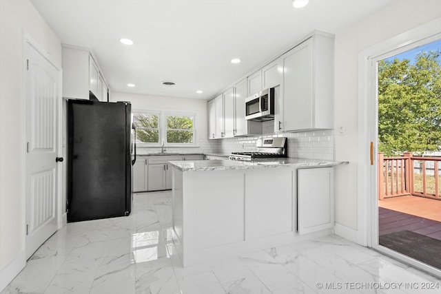 kitchen featuring stainless steel appliances, light stone counters, kitchen peninsula, tasteful backsplash, and white cabinets