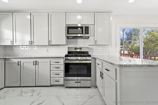 kitchen with white cabinets, appliances with stainless steel finishes, light stone counters, and backsplash