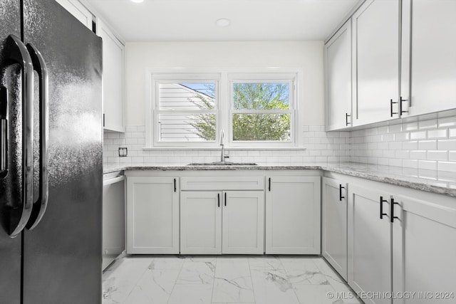 kitchen featuring white cabinets, black fridge, light stone counters, and sink