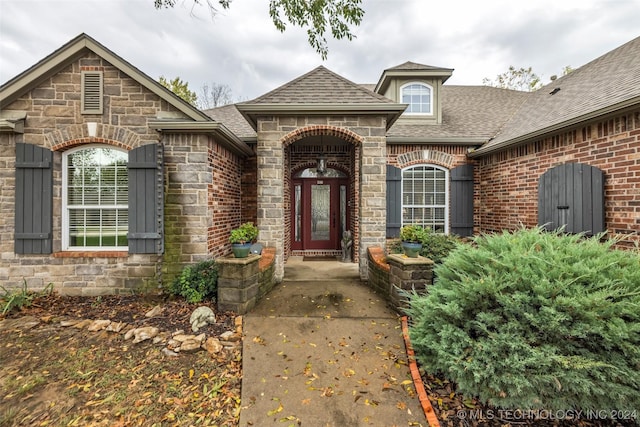 doorway to property with stone siding, brick siding, and roof with shingles