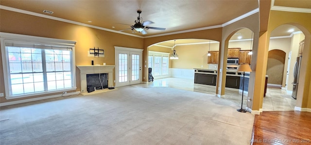 living room with light carpet, a fireplace with raised hearth, a ceiling fan, crown molding, and french doors