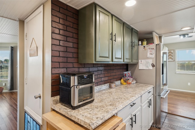 kitchen featuring brick wall, dark hardwood / wood-style floors, light stone counters, and stainless steel refrigerator