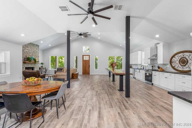 dining space with a stone fireplace, high vaulted ceiling, light hardwood / wood-style flooring, and ceiling fan