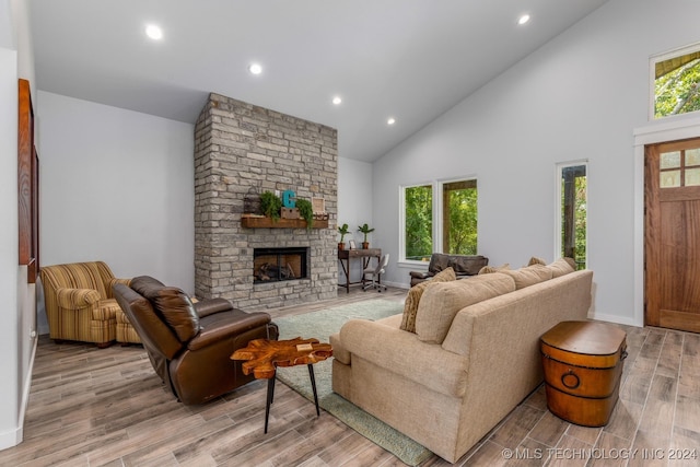 living room featuring a stone fireplace, high vaulted ceiling, and light hardwood / wood-style flooring