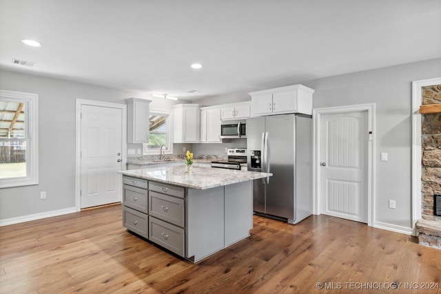 kitchen featuring a center island, appliances with stainless steel finishes, light stone countertops, white cabinets, and light hardwood / wood-style flooring