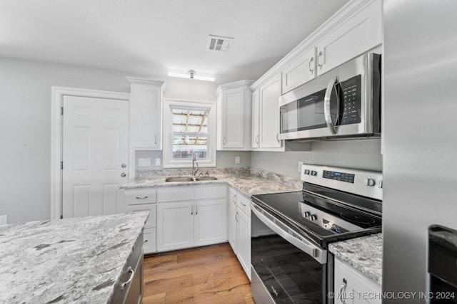 kitchen with sink, light stone counters, appliances with stainless steel finishes, light hardwood / wood-style flooring, and white cabinets