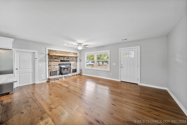 unfurnished living room with wood-type flooring, ceiling fan, and a wood stove