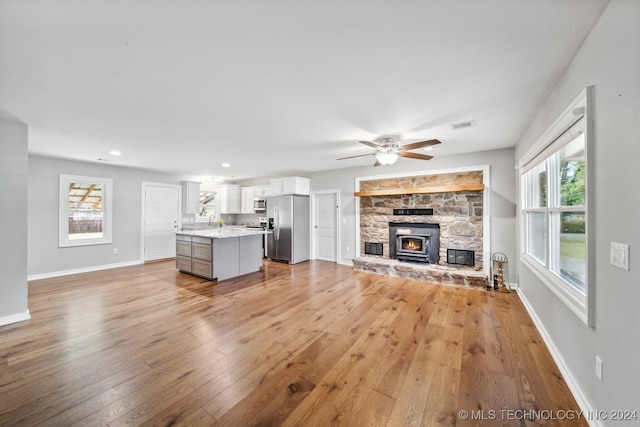 unfurnished living room featuring a wood stove, light hardwood / wood-style flooring, a healthy amount of sunlight, and ceiling fan