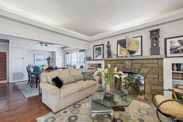 living room with a stone fireplace, dark wood-type flooring, and ceiling fan