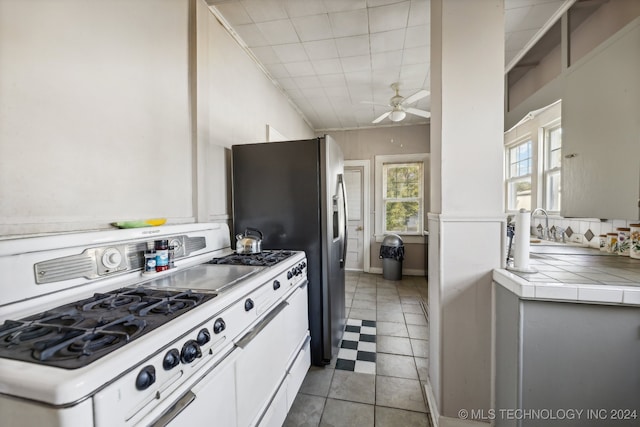 kitchen with tile countertops, white cabinets, light tile patterned floors, ceiling fan, and white gas stove