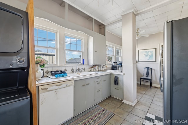 kitchen with stacked washer and clothes dryer, sink, white dishwasher, white cabinets, and stainless steel fridge