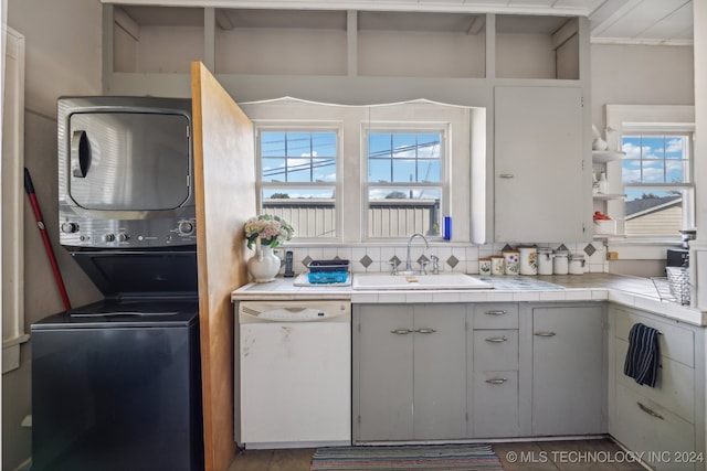 kitchen featuring white dishwasher, stacked washer and dryer, a healthy amount of sunlight, and sink