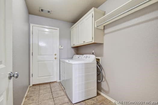 clothes washing area featuring washing machine and dryer, cabinets, and light tile patterned floors