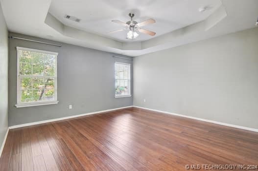 unfurnished room with hardwood / wood-style floors, ceiling fan, and a raised ceiling