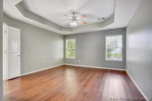 empty room with hardwood / wood-style flooring, ceiling fan, a healthy amount of sunlight, and a tray ceiling