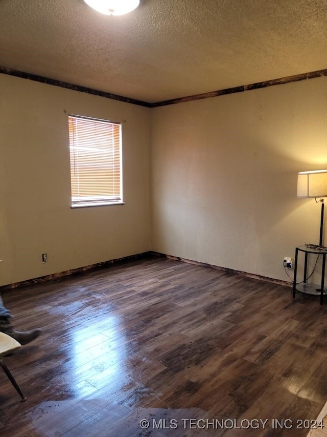 spare room with a textured ceiling, ornamental molding, and dark wood-type flooring