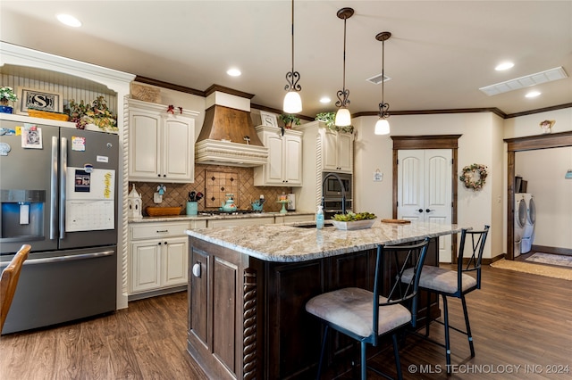 kitchen featuring dark hardwood / wood-style flooring, a center island with sink, hanging light fixtures, appliances with stainless steel finishes, and premium range hood