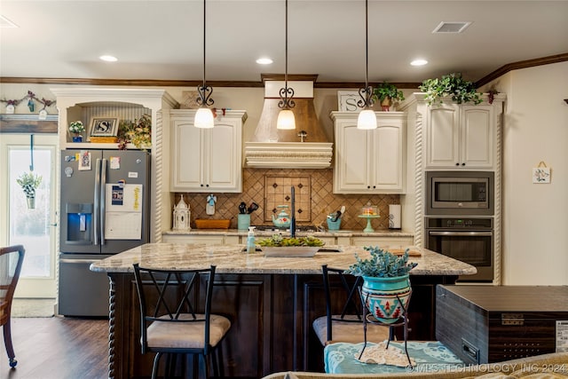 kitchen with hanging light fixtures, light stone countertops, an island with sink, and appliances with stainless steel finishes