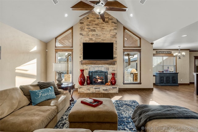 living room featuring a stone fireplace, high vaulted ceiling, hardwood / wood-style floors, and ceiling fan with notable chandelier