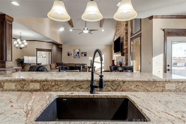 kitchen with sink, light stone counters, ceiling fan with notable chandelier, pendant lighting, and vaulted ceiling