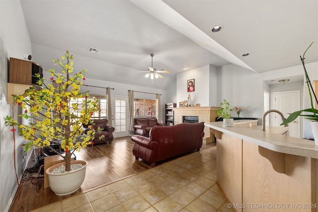 living room featuring ceiling fan, lofted ceiling, wood-type flooring, and a brick fireplace