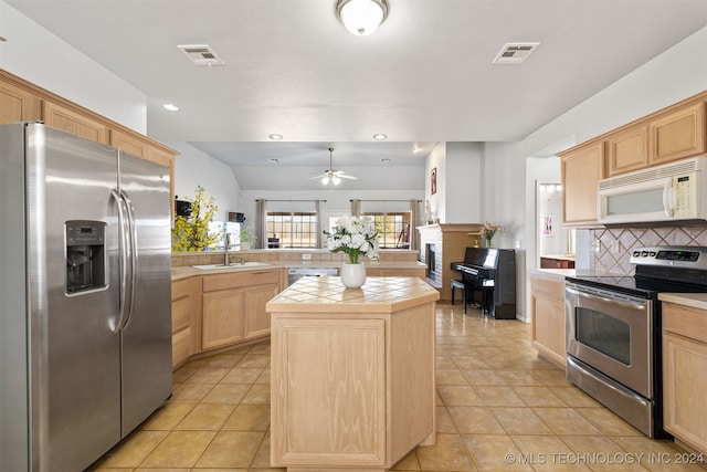 kitchen with light brown cabinets, stainless steel appliances, kitchen peninsula, tile countertops, and a kitchen island