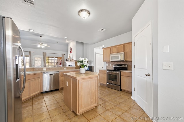 kitchen featuring a center island, backsplash, ceiling fan, light tile patterned floors, and appliances with stainless steel finishes