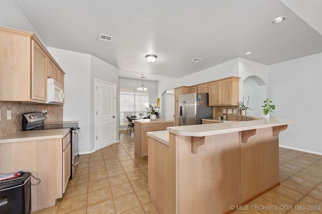 kitchen featuring backsplash, kitchen peninsula, stainless steel appliances, and light brown cabinetry