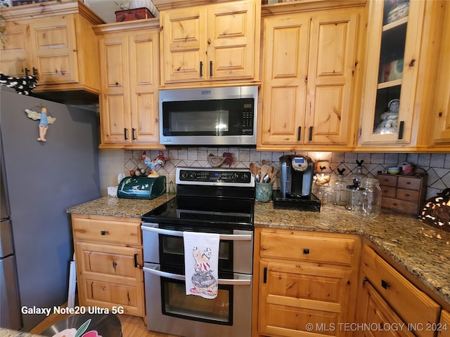 kitchen with light wood-type flooring, stainless steel appliances, light stone counters, and tasteful backsplash