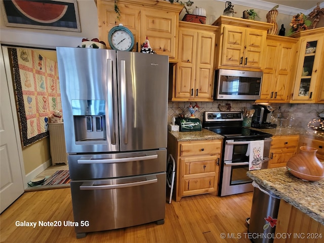 kitchen with tasteful backsplash, light wood-type flooring, appliances with stainless steel finishes, and light stone counters