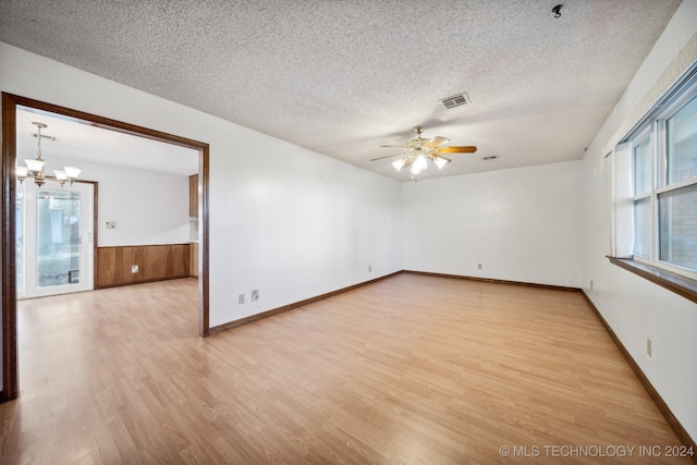 empty room with ceiling fan with notable chandelier, light hardwood / wood-style flooring, and a textured ceiling