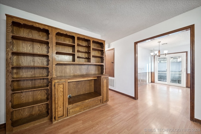 unfurnished living room featuring a chandelier, a textured ceiling, and light hardwood / wood-style flooring