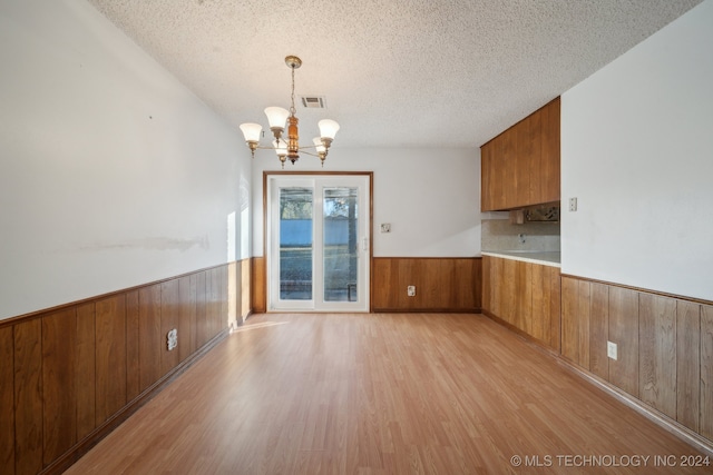 unfurnished dining area featuring light wood-type flooring, wood walls, and a textured ceiling