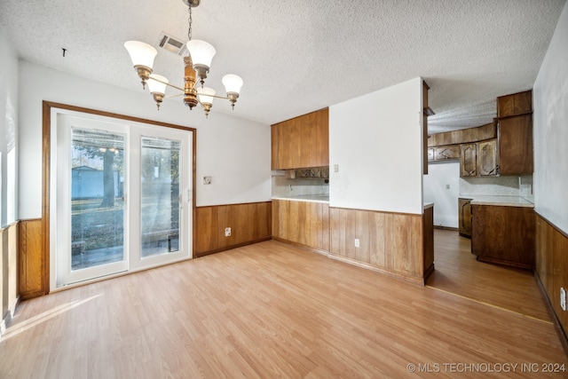 kitchen featuring light hardwood / wood-style floors, kitchen peninsula, a textured ceiling, decorative light fixtures, and a notable chandelier