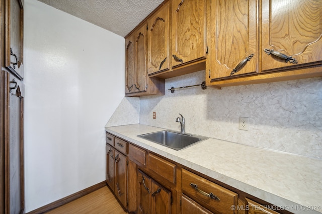 kitchen with a textured ceiling, light hardwood / wood-style flooring, sink, and tasteful backsplash