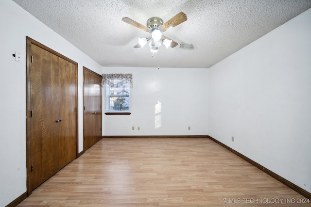 unfurnished bedroom with ceiling fan, a textured ceiling, multiple closets, and light wood-type flooring