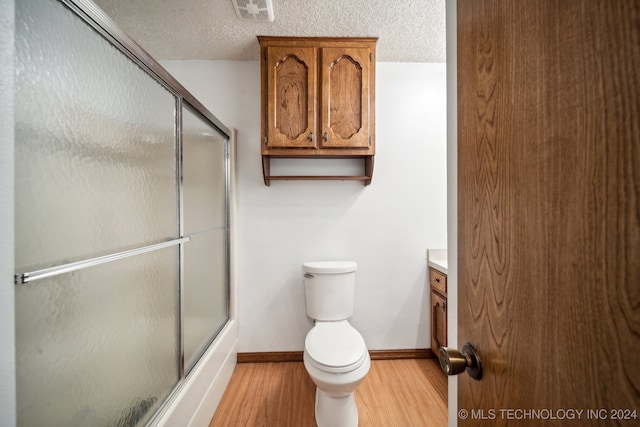 full bathroom featuring wood-type flooring, toilet, a textured ceiling, combined bath / shower with glass door, and vanity