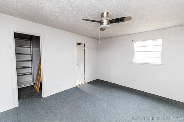 unfurnished bedroom with ceiling fan, a textured ceiling, a walk in closet, dark carpet, and a closet