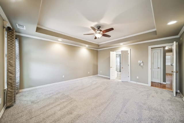 unfurnished bedroom featuring a tray ceiling, light colored carpet, ceiling fan, and crown molding