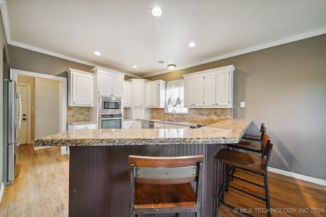 kitchen with white cabinets, a breakfast bar area, light hardwood / wood-style floors, and stainless steel appliances