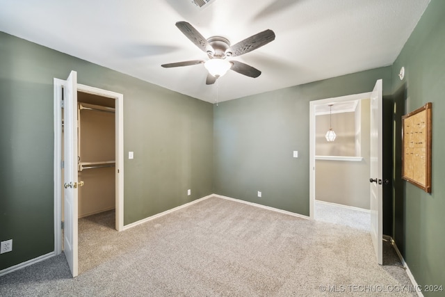 unfurnished bedroom featuring ceiling fan, light carpet, a closet, and a walk in closet