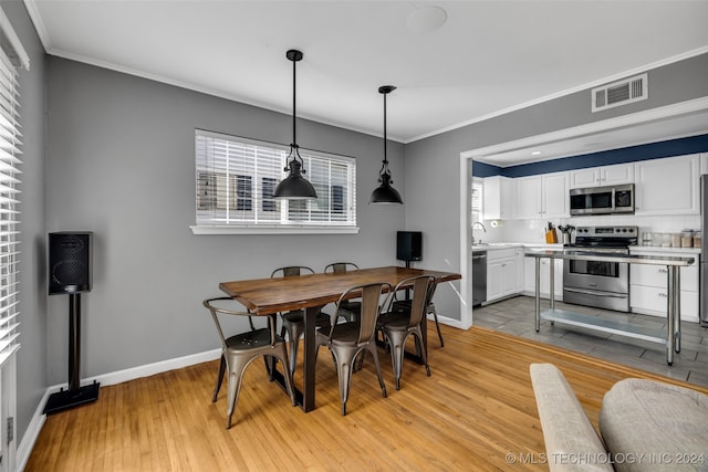 dining space featuring sink, light hardwood / wood-style flooring, and ornamental molding