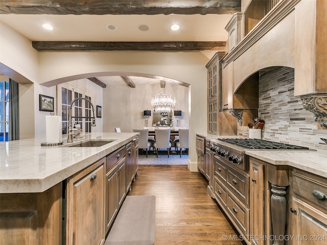 kitchen featuring arched walkways, stainless steel gas stovetop, wood finished floors, and light stone countertops