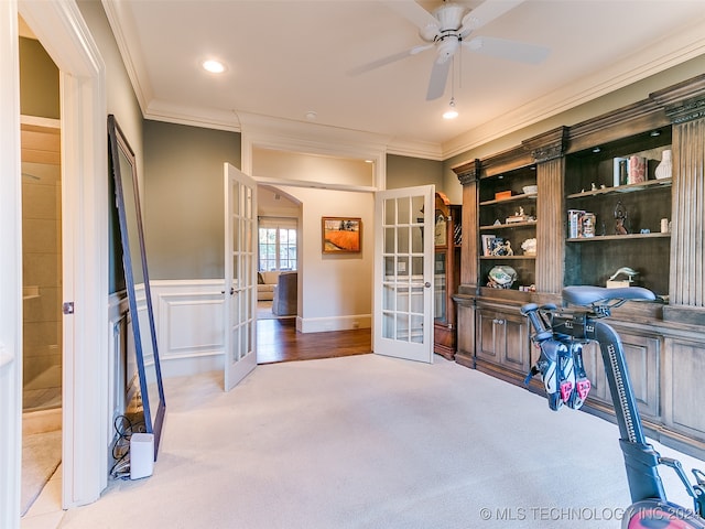 carpeted office space with a ceiling fan, crown molding, french doors, and a wainscoted wall