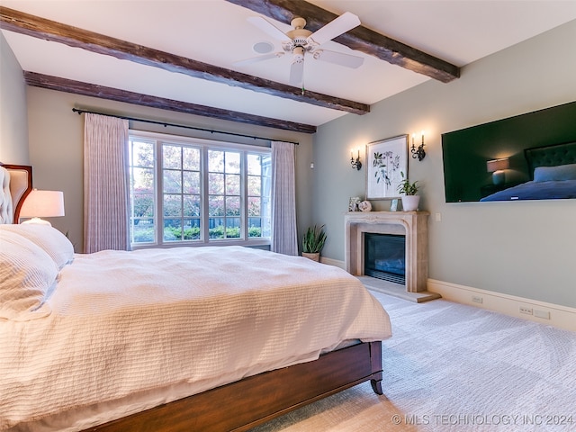 carpeted bedroom featuring a glass covered fireplace, beamed ceiling, a ceiling fan, and baseboards