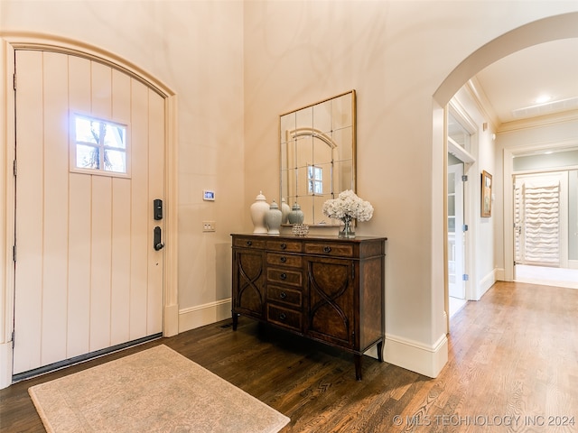 foyer featuring wood finished floors, arched walkways, and baseboards