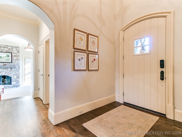 entrance foyer with baseboards, arched walkways, dark wood-type flooring, and a fireplace