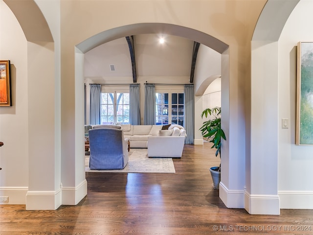 unfurnished living room with vaulted ceiling with beams, baseboards, and wood finished floors