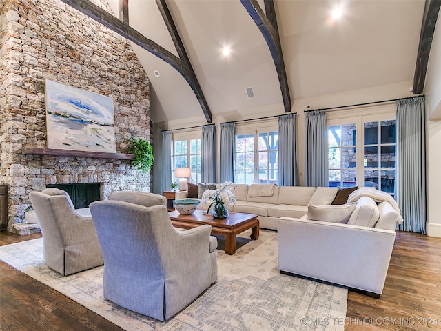 living area with a stone fireplace, beam ceiling, wood finished floors, and high vaulted ceiling